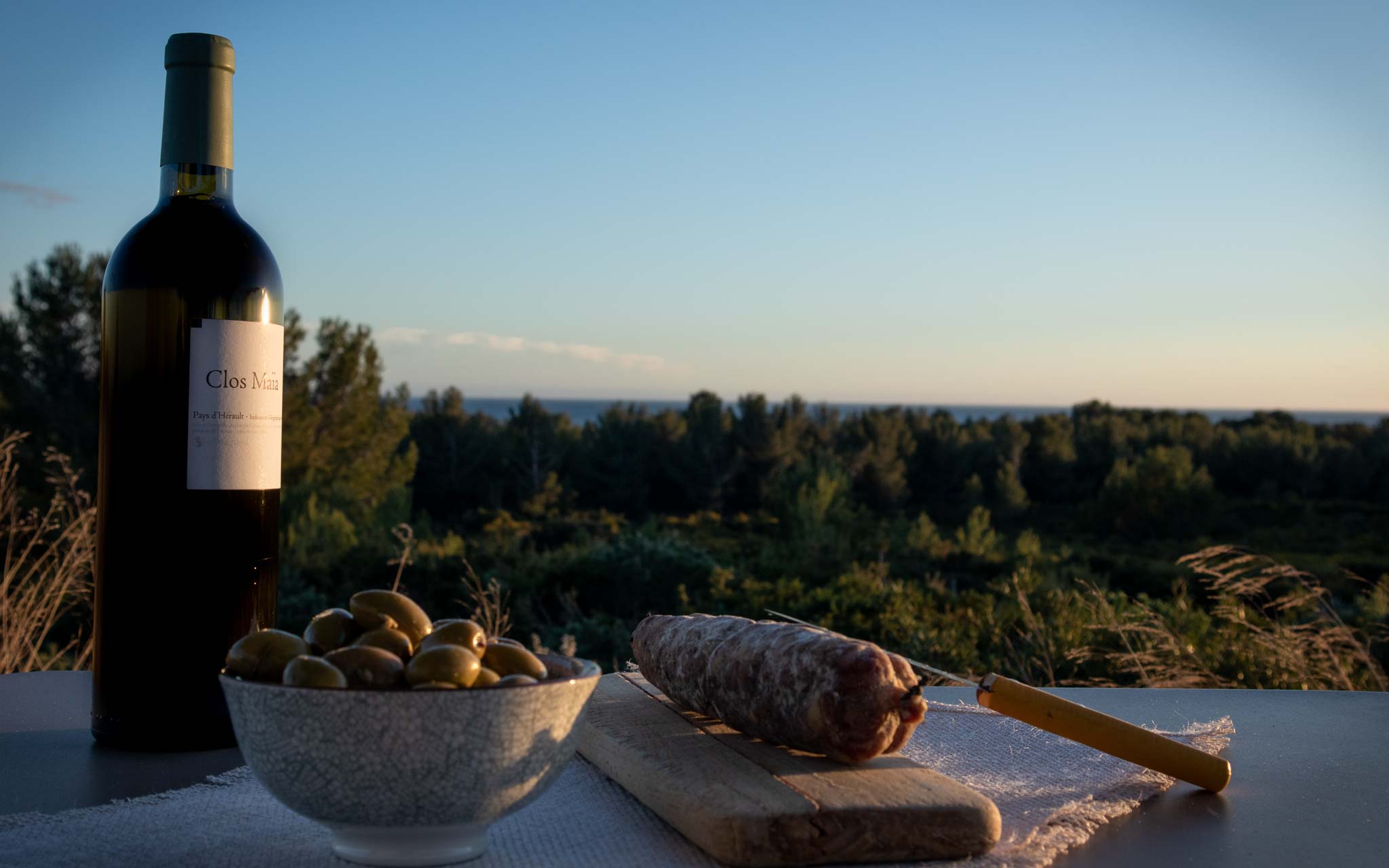 Bouteille de Clos Maïa Blanc un vin des Terrasses du Larzac avec des olives et un saucisson